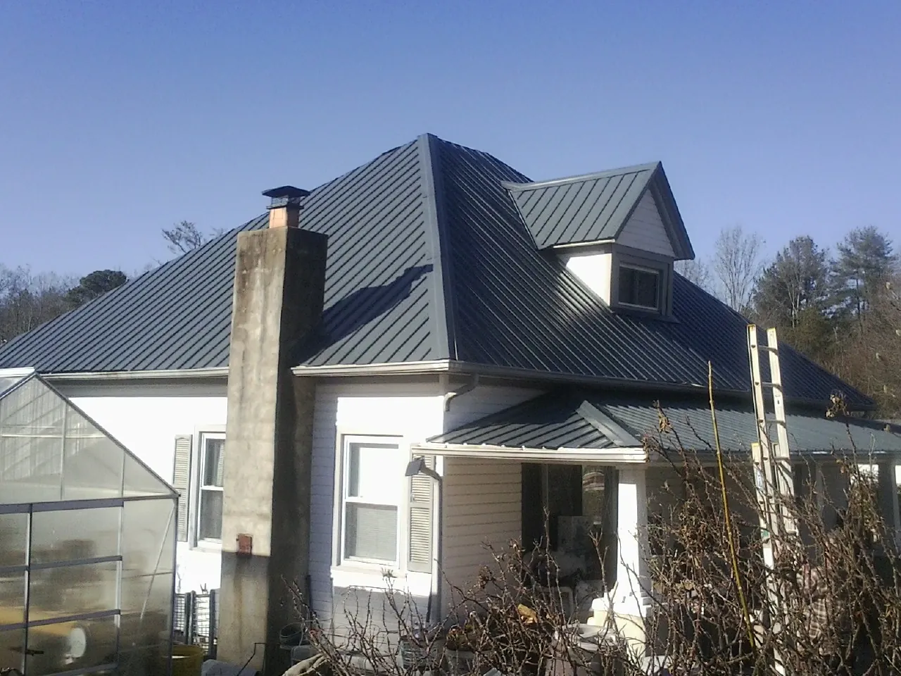Dark blue standing seam metal roof on a white farmhouse with dormer — Slate & Tile Roof Repair by Roofing Brothers in Sandy Lake