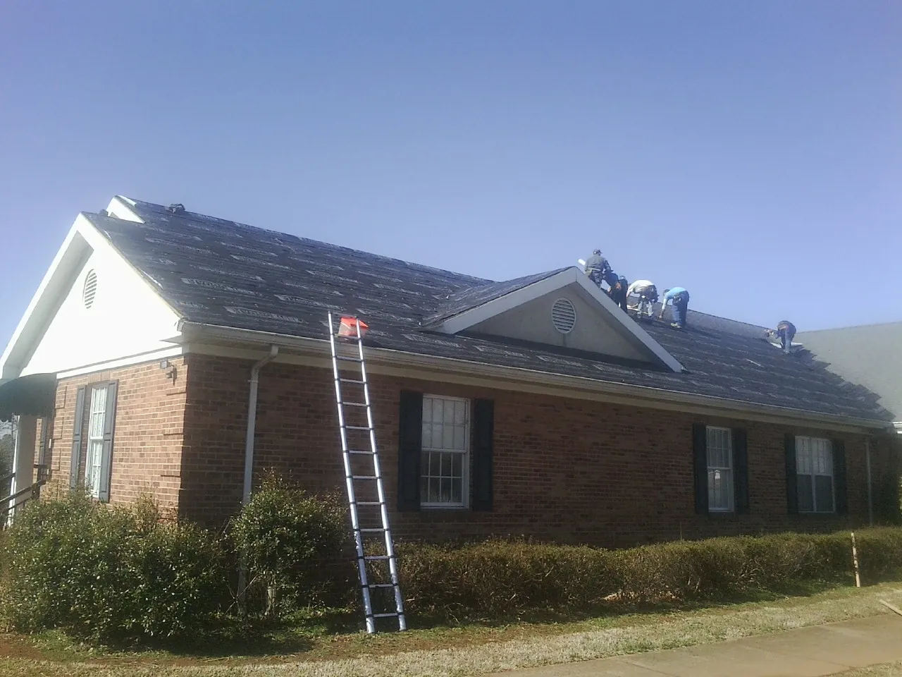 Crew tearing shingles off a brick ranch roof with a ladder set — Emergency Roof Repair work by our crew in Sandy Lake
