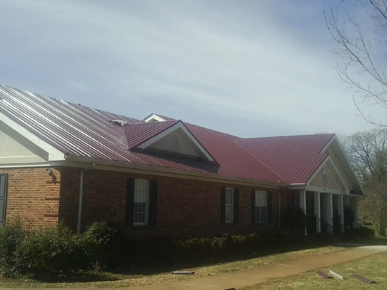 Red metal roof with gabled entries on a long brick building, from a Hail Damage Roof Repair job in Sandy Lake