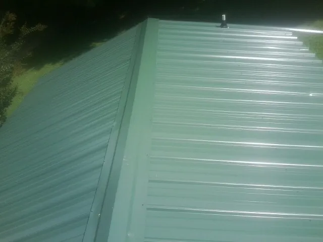 New green metal panels meeting at the ridge of a roof — Flat Roof Repair work by our crew in Sandy Lake