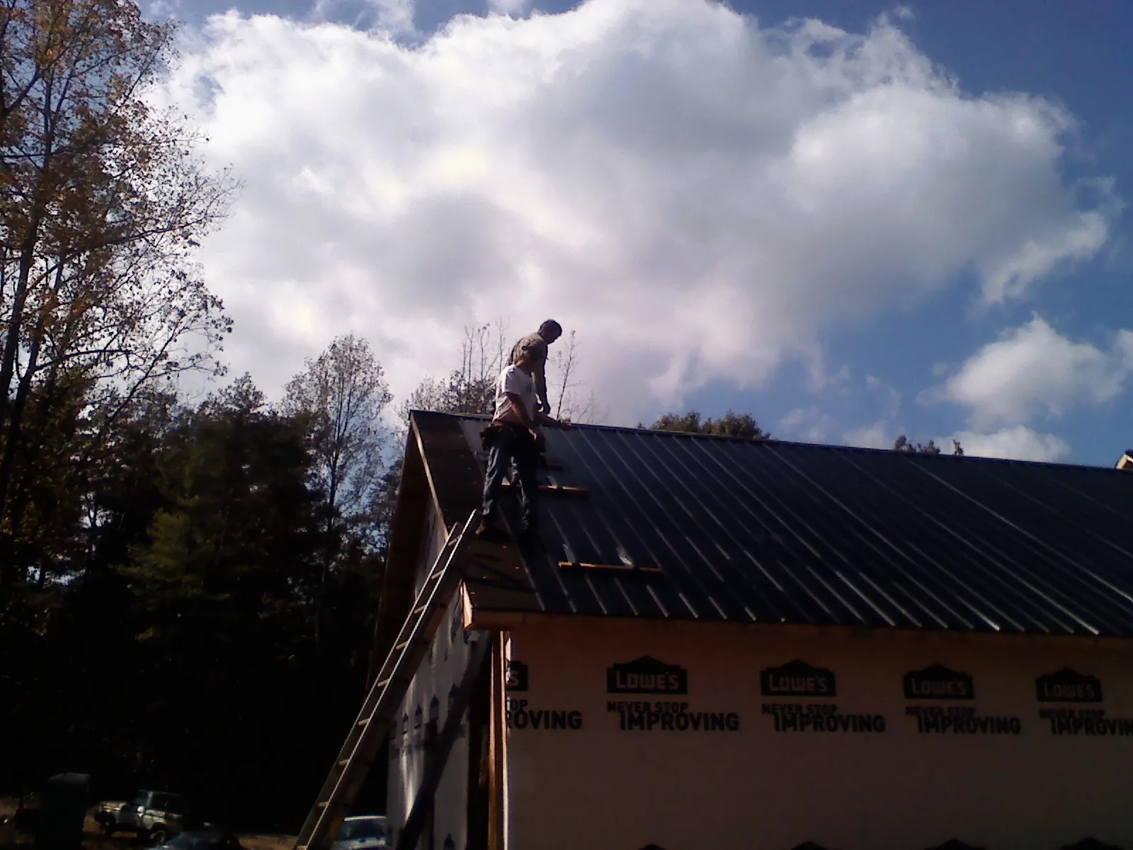 Roofer fastening dark metal panels high against a cloudy sky, from a Roof Inspection job in Sandy Lake