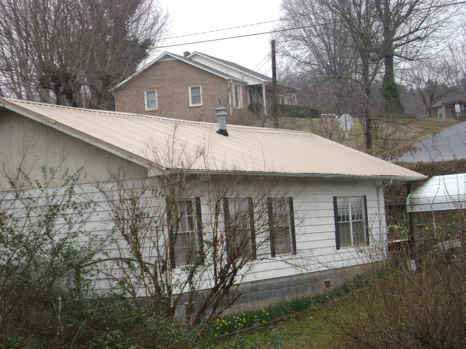 Tan metal roof on a white sided house set into a hillside — Commercial Roofing by Roofing Brothers in Sandy Lake