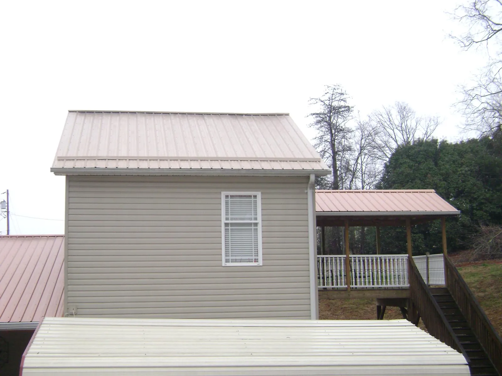 Tan metal roofs on a two story addition and attached porch, from a Roof Replacement job in Sandy Lake